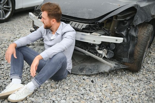 Man sitting next to wrecked car after car accident